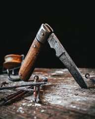 Isolated old pocket knife sticking in a wooden plate with rusty nails in foreground