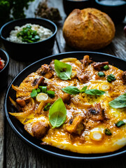 Delicious breakfast - scrambled eggs with fried champignon, cottage cheese and vegetable served on black plate on wooden table
