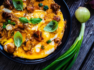 Delicious breakfast - scrambled eggs with fried champignon, cottage cheese and vegetable served on black plate on wooden table
