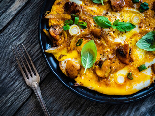 Delicious breakfast - scrambled eggs with fried champignon, cottage cheese and vegetable served on black plate on wooden table
