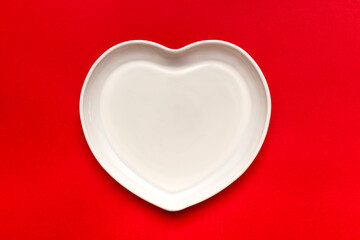Heart shaped plate. Ceramic tableware. On a red background.