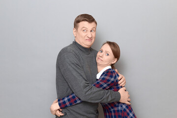 Studio portrait of funny couple hugging and looking disgruntled