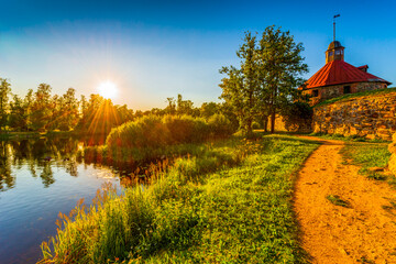 Naklejka premium Medieval fortress on the river bank. Sunset. Woodland. Blue sky. The road near the fortress wall. Beautiful nature. Korela Fortress, Priozersk, Russia. View from the side of the road.