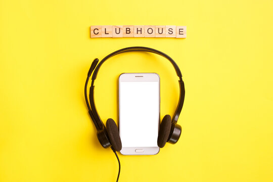Headphones and smartphone with wooden letters on a yellow background. Clubhouse social media concept. Mock up, copy space, flat lay, top view