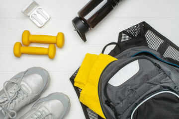 Sports bag, towel, headphones, dumbbells, bottle and sneackers on a white wooden background. Top...