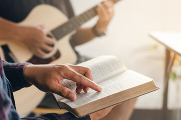 A young boy sat and read the Bible while his friend played guitar at church when he worshiped God. A small group of Christians or a concept in a church at a church