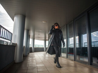 Woman in black leather coat and glasses walks in hurry from building of business center