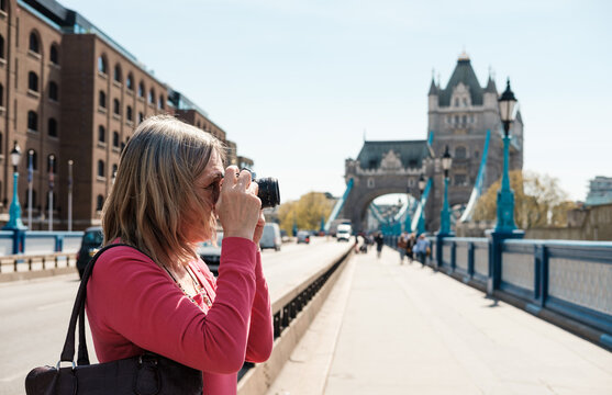 Mature blonde woman taking a picture near tower bridge. She is using a film camera.