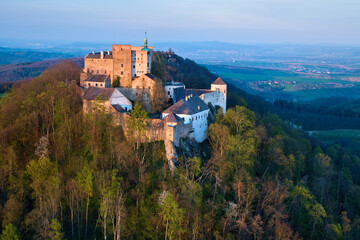 Fototapeta na wymiar Buchlov Castle. Aerial view on monumental castle in Romanesque Gothic style, standing on a wooded hill against Saint Barbara’s Chapel on the hill in background. Spring, tourism hot spot. Czech castles