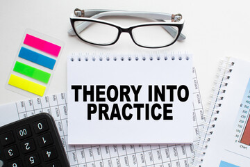 Notepad with text THEORY INTO PRACTICE on the office desk with stationery. A blank notepad for entering a copy or text. business