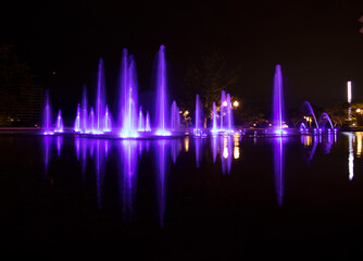 Long exposure of a colourful outdoor water fountain at night - illuminated purple fountains