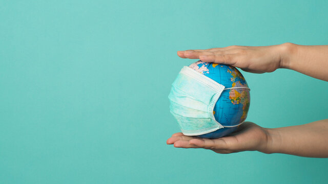 Hands is holding earth globe and face mask on mint green or Tiffany Blue background.covid-19 concept.