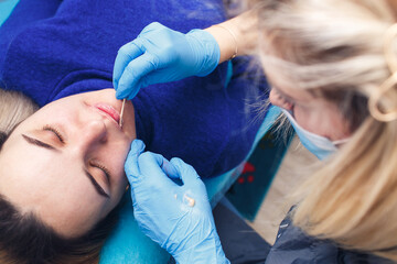 beautician applies an anesthetic to the lips before performing permanent makeup.