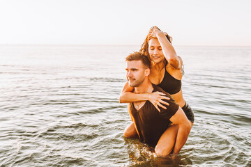 Happy young fit couple embrace each other with love in the sea or ocean at summer sunset. Romantic mood, tenderness, relationship, vacation concept.