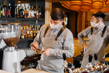 Two masked baristas prepare delicious coffee in the cafe bar. The work of restaurants and cafes during the pandemic.