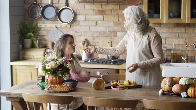 long haired lady breastfeeds little baby sitting at brown wooden table eating pice of pumpkin from mother hands.and talking Family spending time together in chalet 