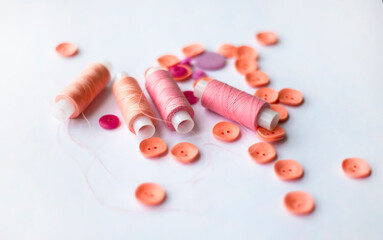 A scattering of buttons and threads of coral and pink color on a white background. Copy space for text.