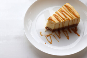 Piece of new york baked cheesecake with caramel sauce on plate on white table background. Close-up of cheese cake with topping. Top view