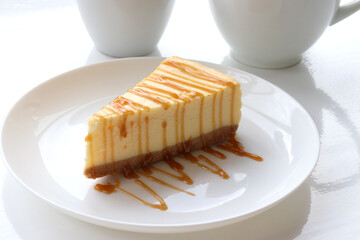 Piece of new york baked cheesecake with caramel sauce on plate on white table background. Close-up...