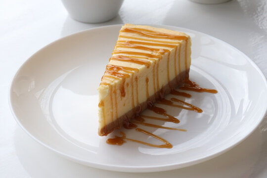 Piece of new york baked cheesecake with caramel sauce on plate on white table background. Close-up of cheese cake with topping. Top view