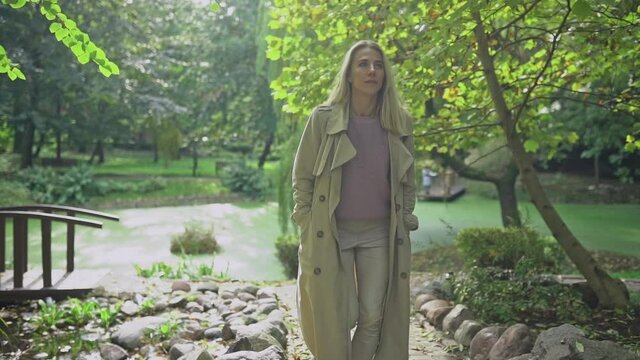 Clow motion footage of caucasian blonde woman smiling happily on sunny summer or spring day outside walking in park.