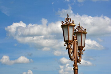 Fototapeta na wymiar Electric street lamp exclusive shape, metal and glass, close-up against a blue cloudy sky