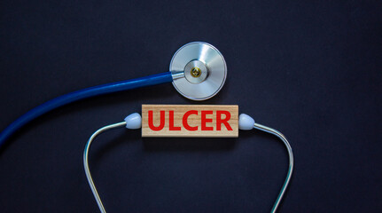 Ulcer symbol. Wooden block with the word 'ulcer' and stethoscope on beautiful black background. Medical and ulcer concept.
