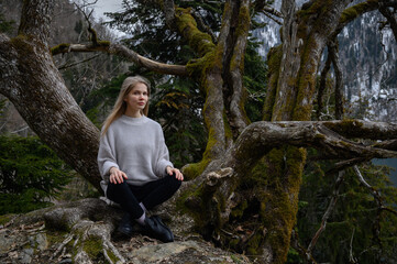 Girl sits on a tree and meditates on blue lake background. Lake Ritsa in Abkhazia