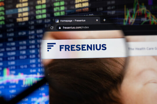 Fresenius company logo on a website with blurry stock market developments in the background, seen on a computer screen through a magnifying glass