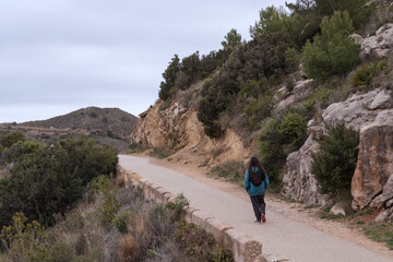Young adult walks a mountain trail with a backpack.