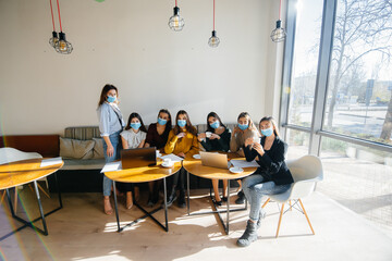 A group of girls in masks sit in a cafe and work on laptops. Teaching students.