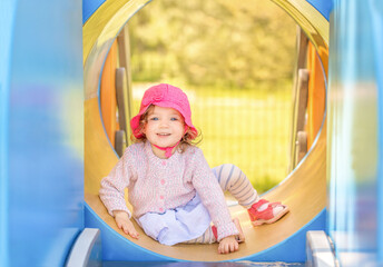 Happy child playing on outdoor playground in summer. Little girl plays on school or kindergarten yard. Healthy summer activity for children.