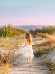Little girl running along wooden path towards seaside.