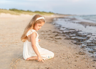 Little beautiful girl with long hair sitting at the seaside.