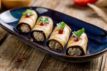 Eggplant rolls stuffed with nuts on blue plate on old wooden table