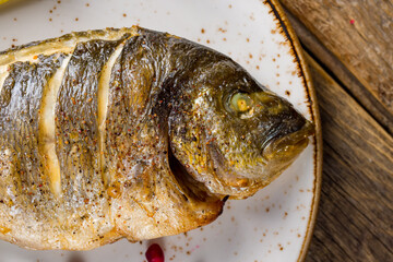 Dorado on grill on a white plate  with lemon and pomegranade on old wooden table top view