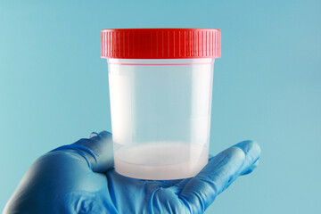 A doctor's hand in a blue disposable medical glove holds a sperm analysis jar against a blue medical background. Laboratory and concept of sperm analysis and donation.Copyspace