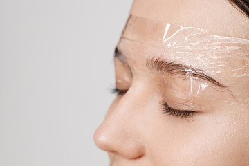 Master applies brow paste with a brush to eyebrows. Styling and lamination of eyebrows. Woman doing...