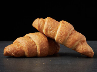 baked french croissants on a brown kitchen board, black background, close-up