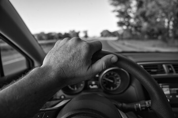 Grayscale shot of a male hand on a steering wheel of a car