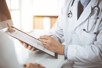Unknown male doctor and patient woman discussing current health examination while sitting in sunny...