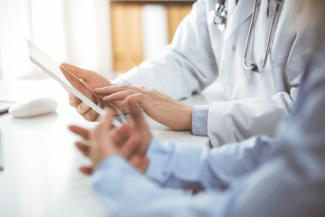 Unknown male doctor and patient woman discussing current health examination while sitting in sunny clinic and using tablet computer. Perfect medical service in hospital