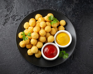 Crispy potato balls with ketchup and mustard on black plate