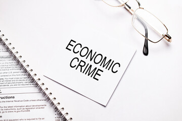 Business concept. Notebook with text ECONOMIC CRIME sheet of white paper for notes and glasses in the grey background