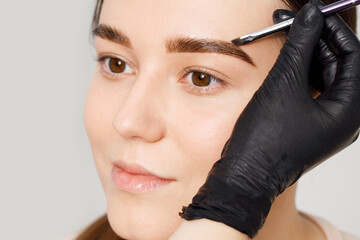 Master applies brow paste with a brush to eyebrows. Styling and lamination of eyebrows. Woman doing...