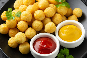 Crispy potato balls with ketchup and mustard on black plate