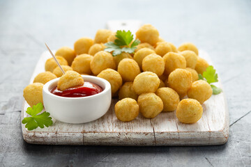 Crispy potato balls with ketchup on white wooden board