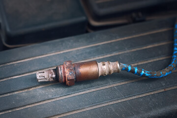 Replace gasoline car oxygen sensor. Old and damaged O2 oxygen, check lambda sensor, close up of engine spare parts. Part of exhaust system of car with combustion engine