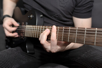 Fototapeta na wymiar A man playing black electric guitar. Guitar fretboard close-up. Learning to play the guitar. Hand grips chords,