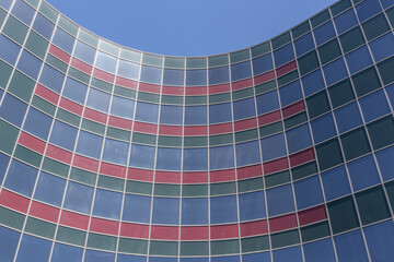 Curved geometric architecture. Blue building with red and green windows against blue sky.